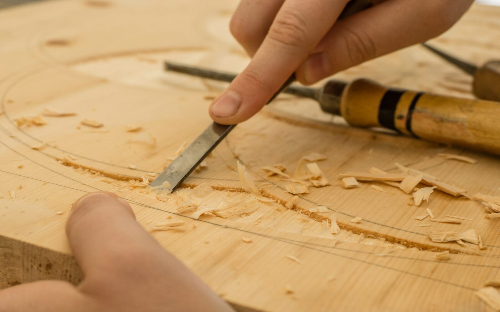 Hands using a chisel on a wood surface.